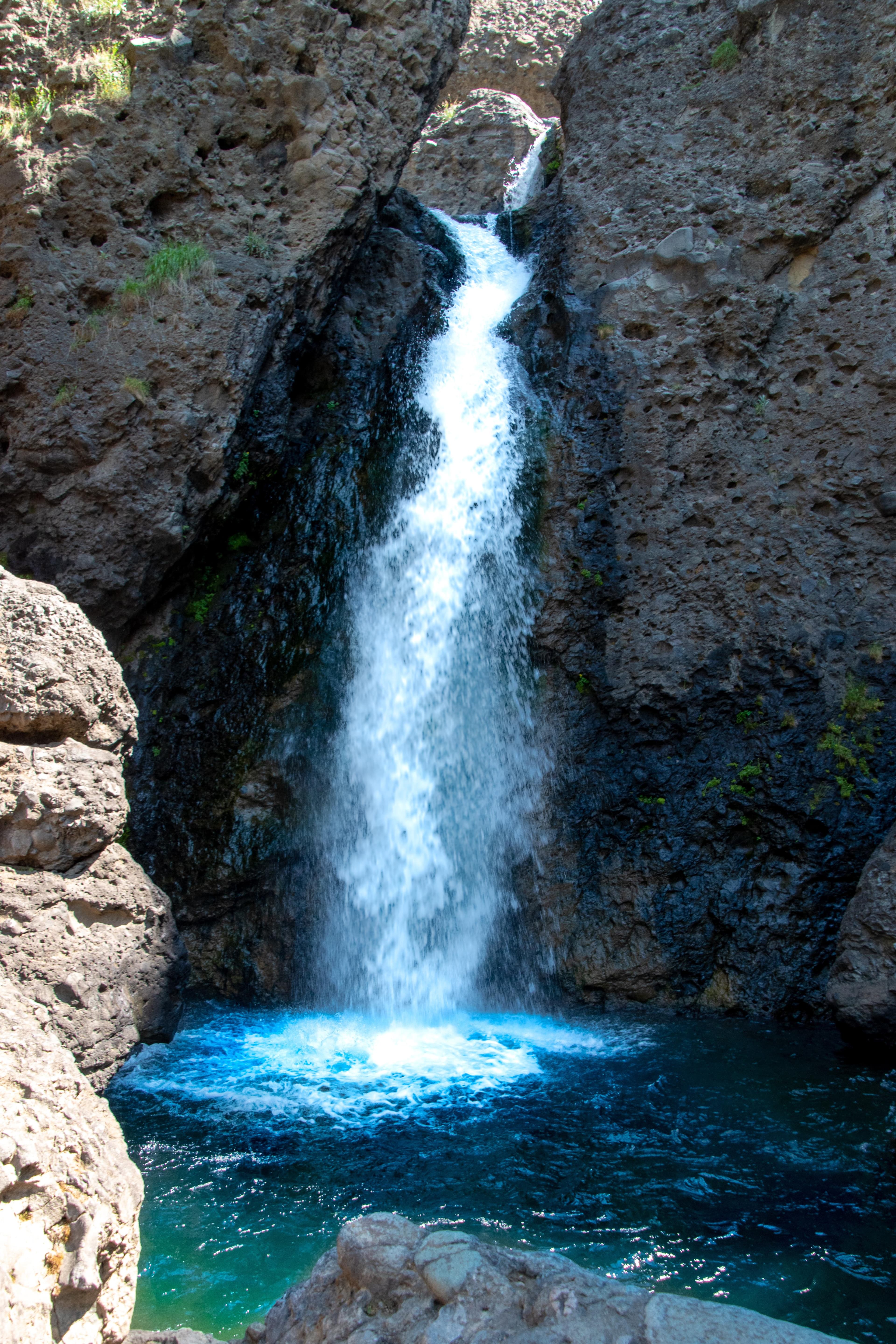 A waterfall falling into a bright blue pool between canyon rocks